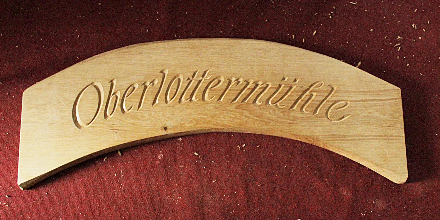 In eine gebogene Eichenleiste geschnittener Schriftzug in Antiqua-Kapitälchen