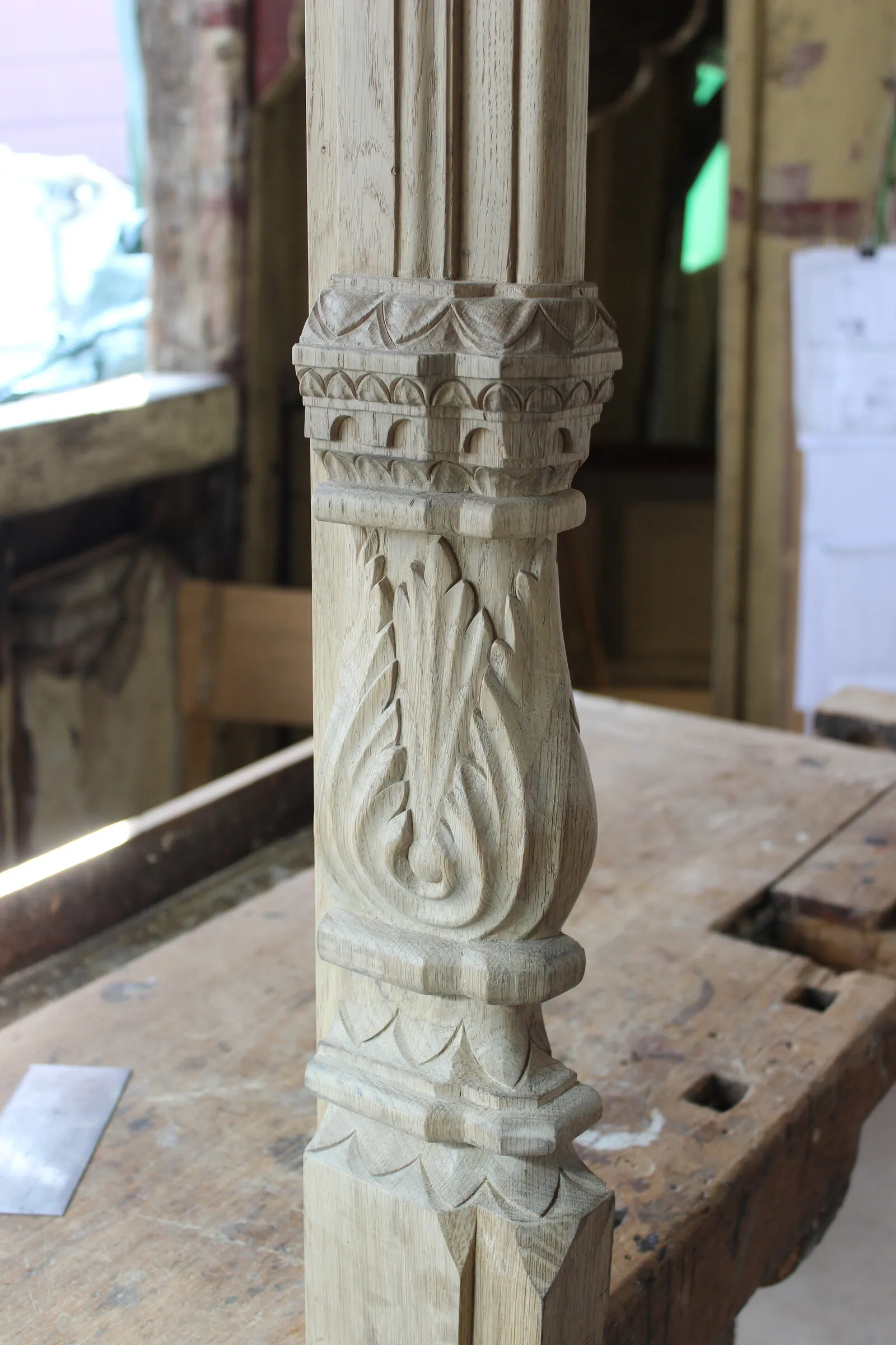 Frisch geschnittenes Kapitell mit Akanthusblatt vor dem stark verwitterten historischen Holz