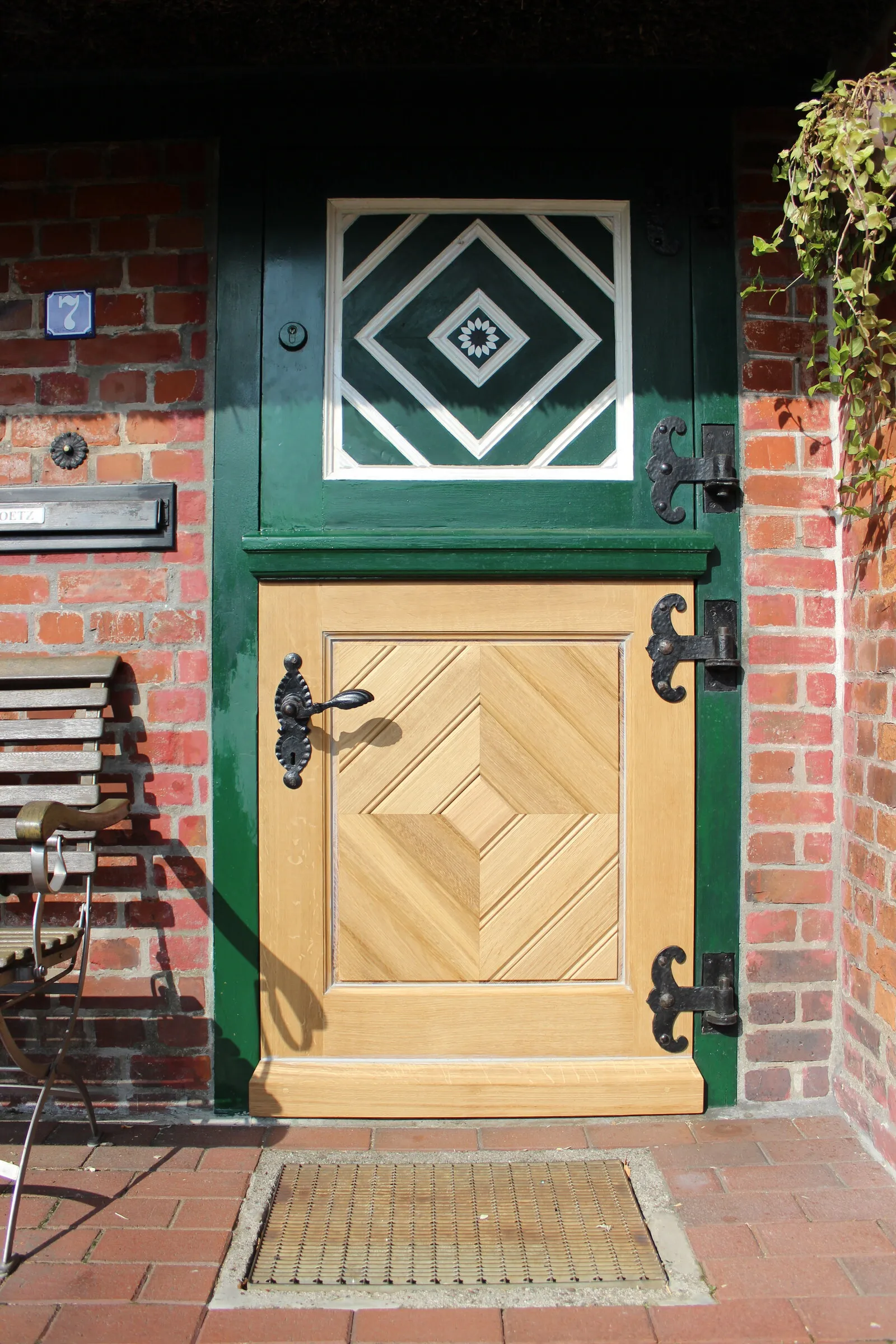Zweigeteilte Klöntür in Eiche mit Rautenfüllung und schmiedeeisernen Bändern, im grünen Rahmen einer Backsteinfassade